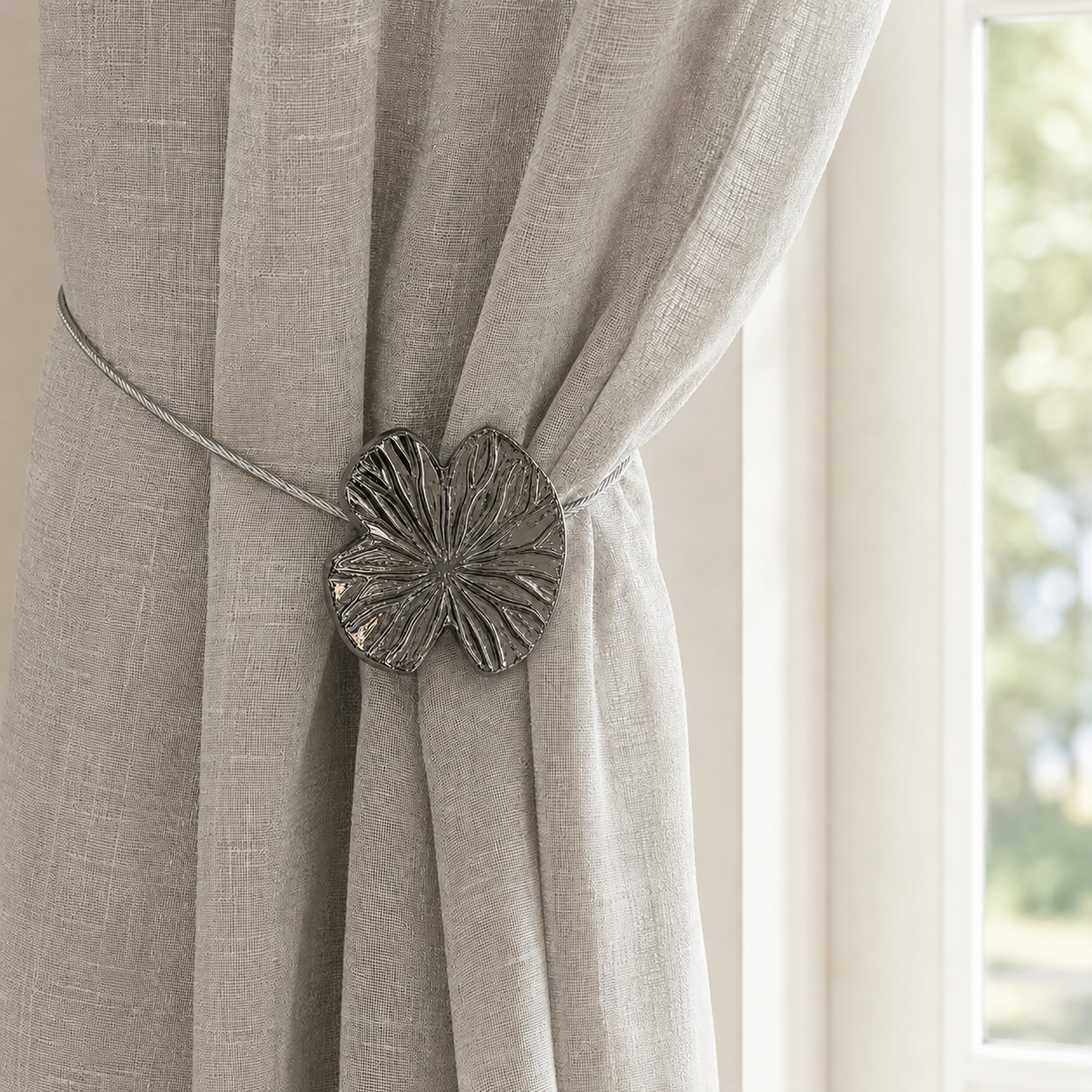 Lifestyle grège: Polished graphite water lily magnetic tieback holding a light gray sheer linen curtain by a sunlit window