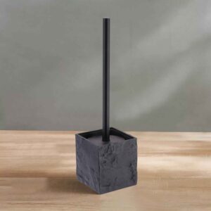 A black stone-effect toilet brush holder from the accessory set, displayed on a wooden surface against a soft green wall.