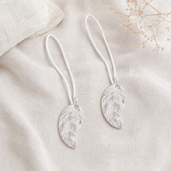 Set of 2 white leaf magnetic curtain tiebacks resting together on natural linen