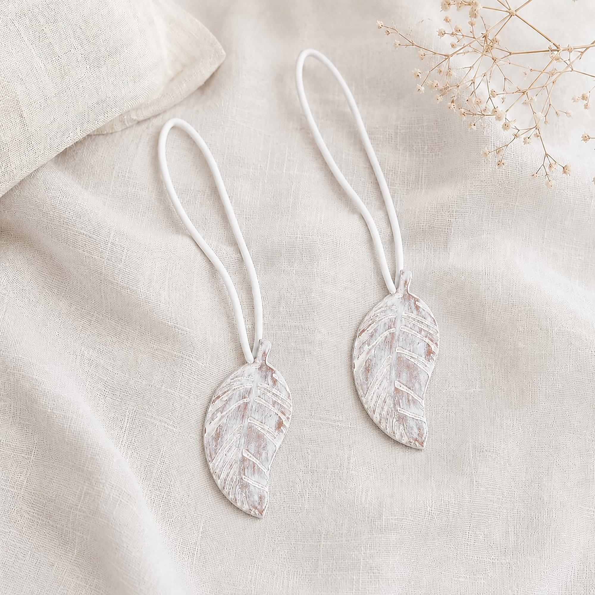 Set of 2 white leaf magnetic curtain tiebacks resting together on natural linen