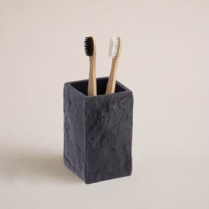 A black stone-effect bathroom tumbler holding two bamboo toothbrushes, displayed against a neutral background for a clean and natural look.
