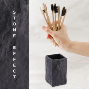 A close-up of a black stone-effect bathroom tumbler next to a hand holding multiple bamboo toothbrushes, emphasizing its modern design and practicality.