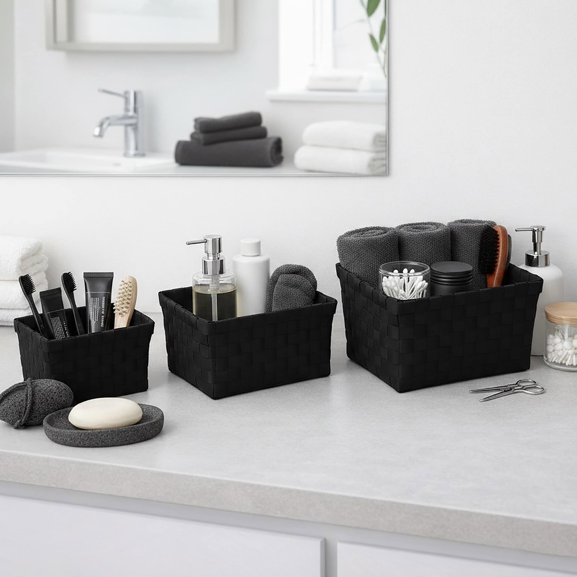 Three black woven strap baskets filled with toothbrushes, skincare bottles, rolled towels, and bath accessories on a bathroom countertop.