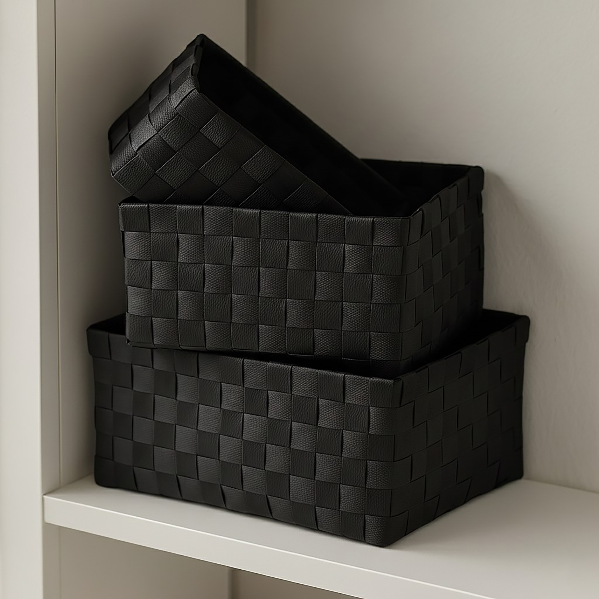 Two black woven strap baskets stacked on a white shelf, shown empty.