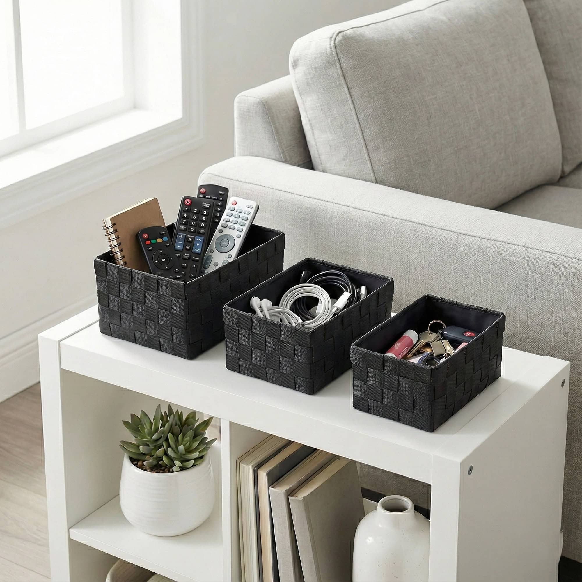 Three black checkered woven strap storage baskets on a side table, holding TV remotes, charging cables, and small accessories.