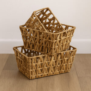 Three natural water hyacinth flared baskets stacked empty on a wood floor against a white wall.
