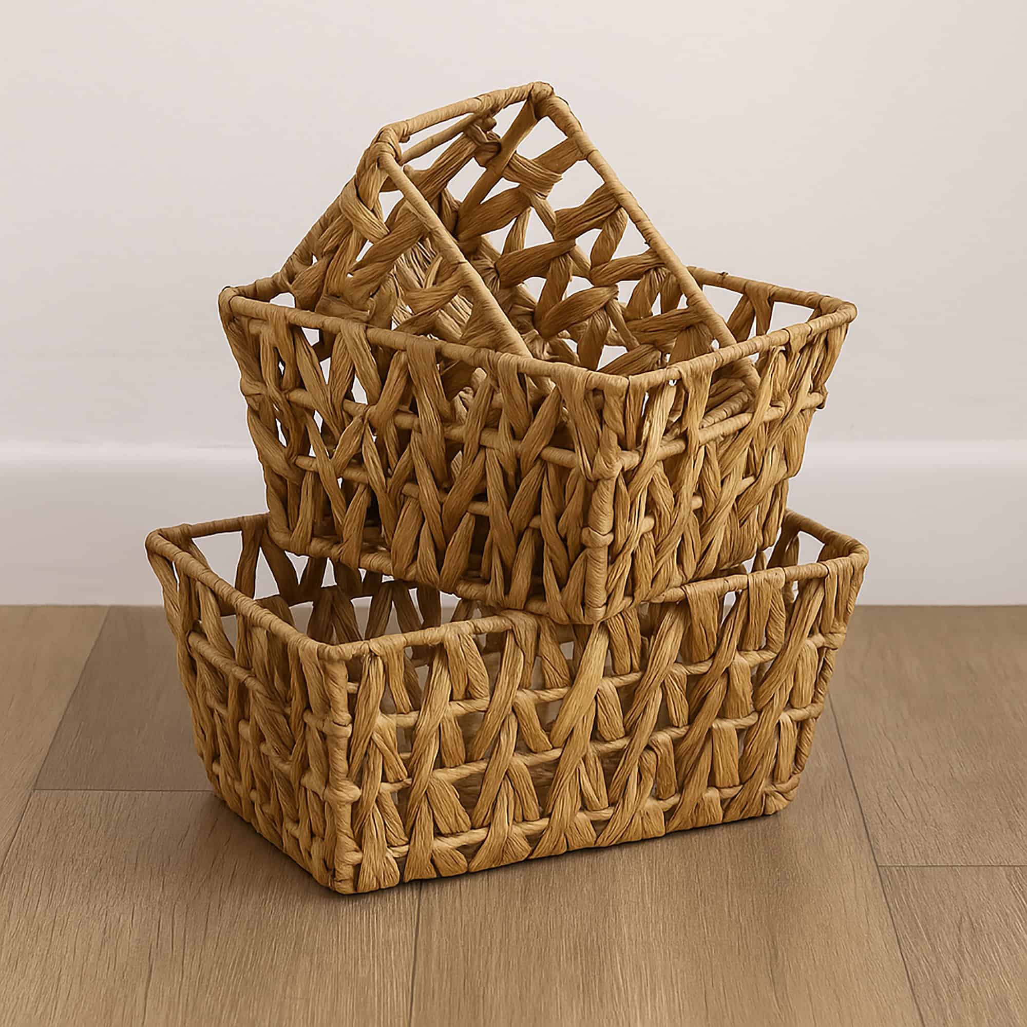 Three natural water hyacinth flared baskets stacked empty on a wood floor against a white wall.