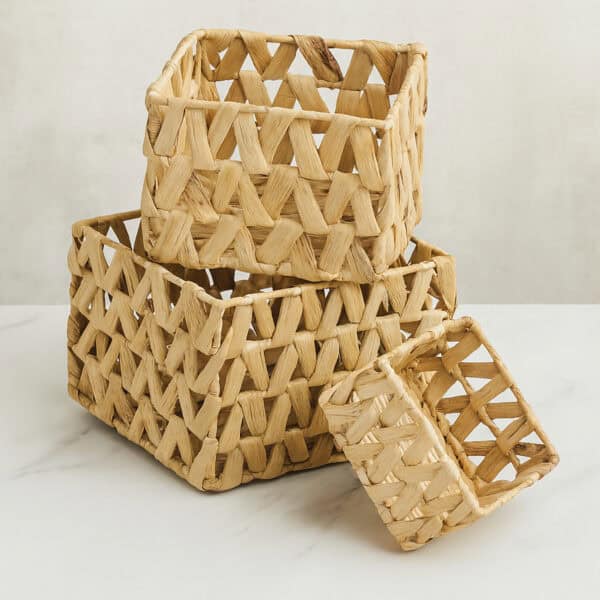 Three natural water hyacinth rectangular baskets stacked empty on a marble surface against a gray wall.