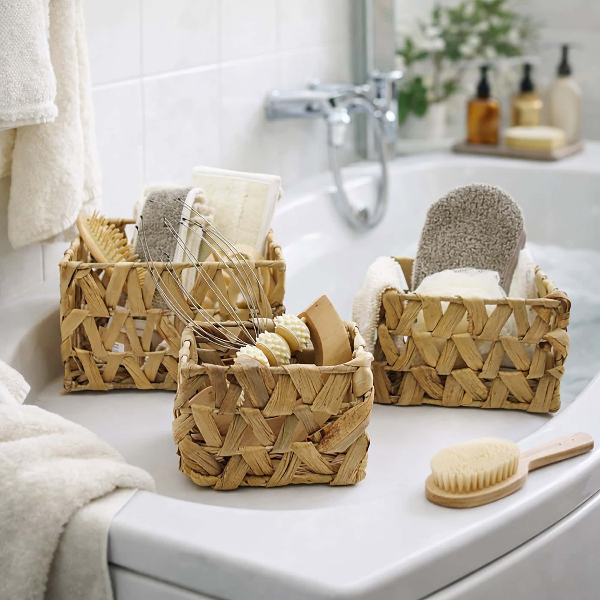 Three water hyacinth baskets filled with bath brushes, loofahs, and spa accessories displayed on a bathtub ledge.