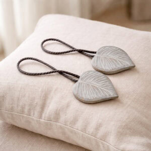Gray wooden leaf tiebacks with gray cord on linen cushion
