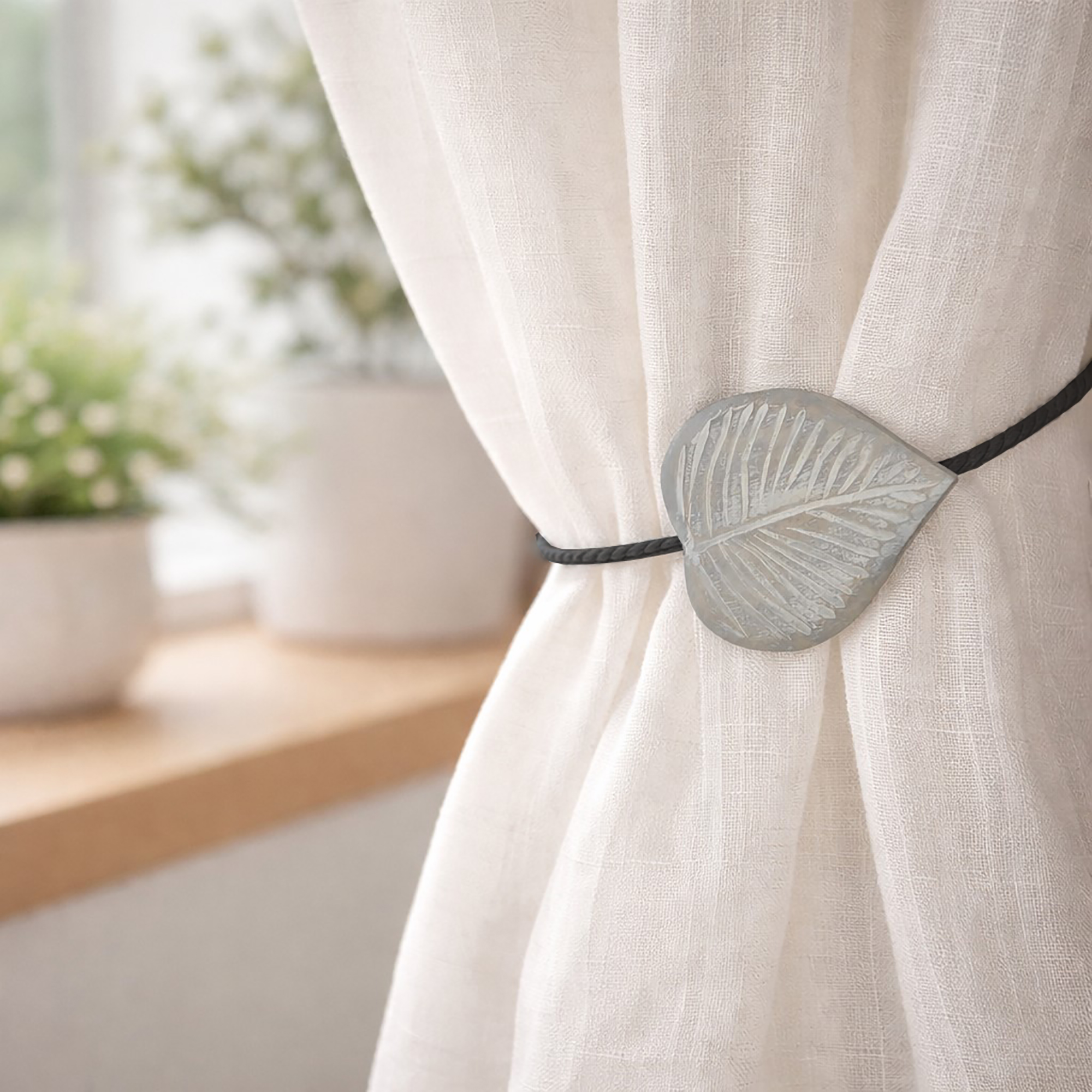 Gray carved leaf tieback holding sheer curtain by bright window