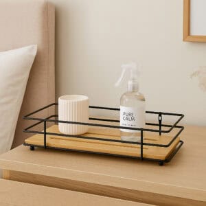 "Black metal wire bamboo tray with candle and spray bottle on wooden nightstand"