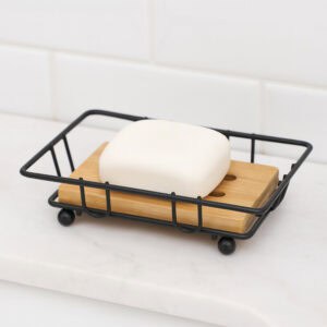 "White bar soap on black wire and bamboo dish on white counter"