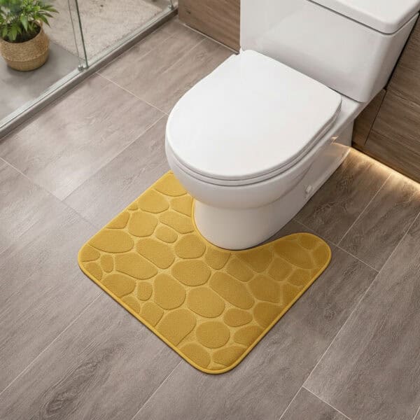 Mustard yellow memory foam contour bath mat with pebble texture positioned around toilet base, angled view