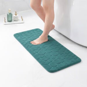 Barefoot stepping on a long peacock blue runner mat with pebble texture placed on a bathroom tile floor next to a tub