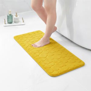 Barefoot stepping on a long mustard yellow runner mat with pebble texture placed on a bathroom tile floor next to a tub