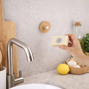 "Hand placing soap with magnet near bamboo holder mounted on kitchen wall"