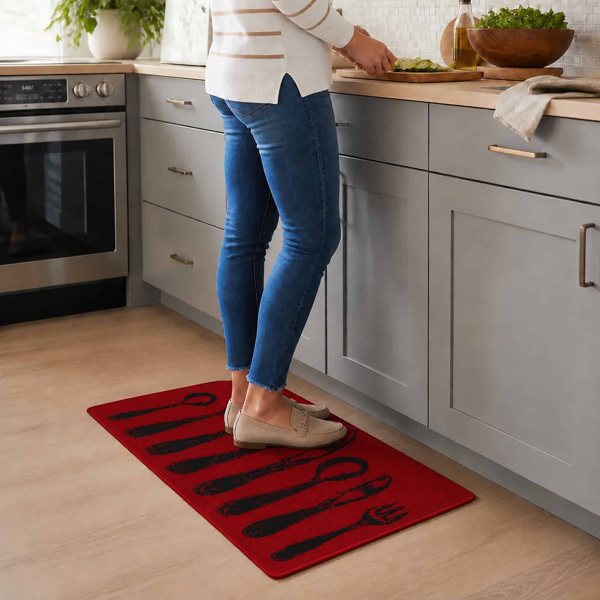 Person in jeans standing on a red cutlery print kitchen rug while prepping food at a gray counter, showing the mat in a real kitchen.