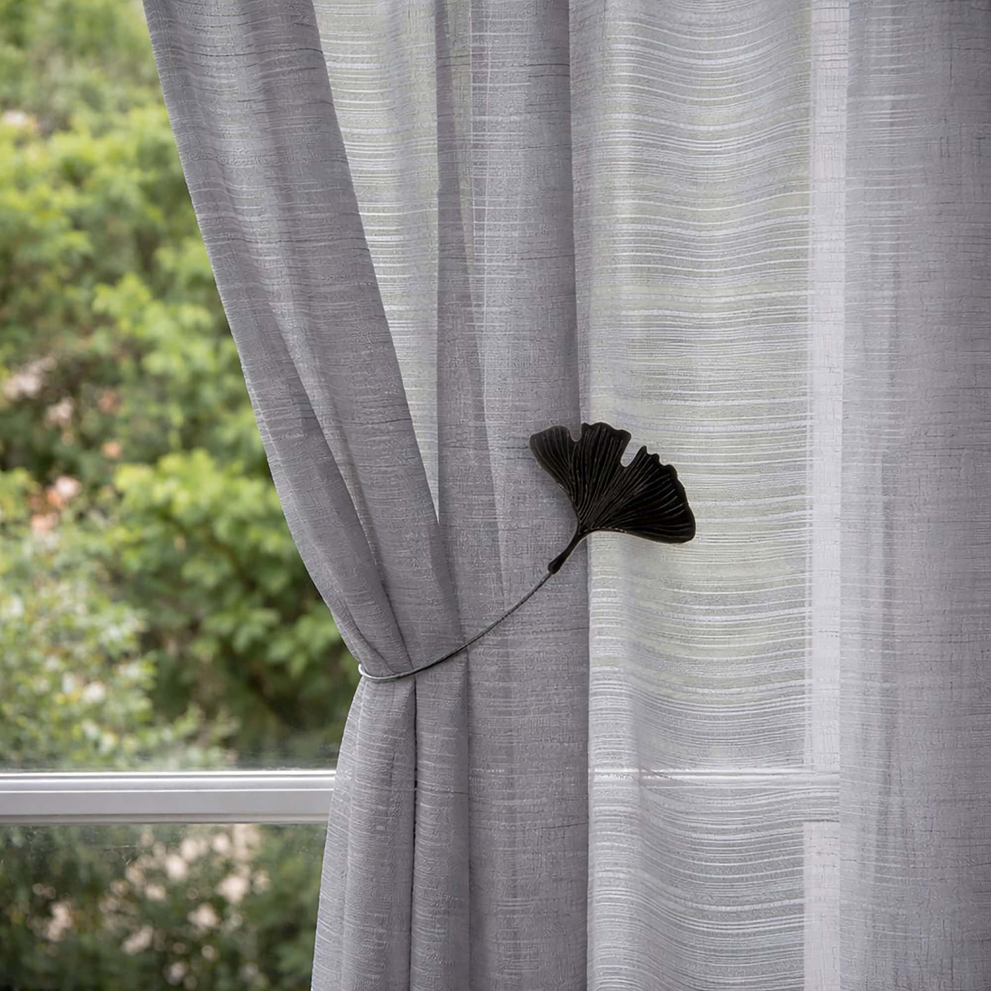 "Black ginkgo leaf magnetic tieback on grey textured curtains beside a garden window"