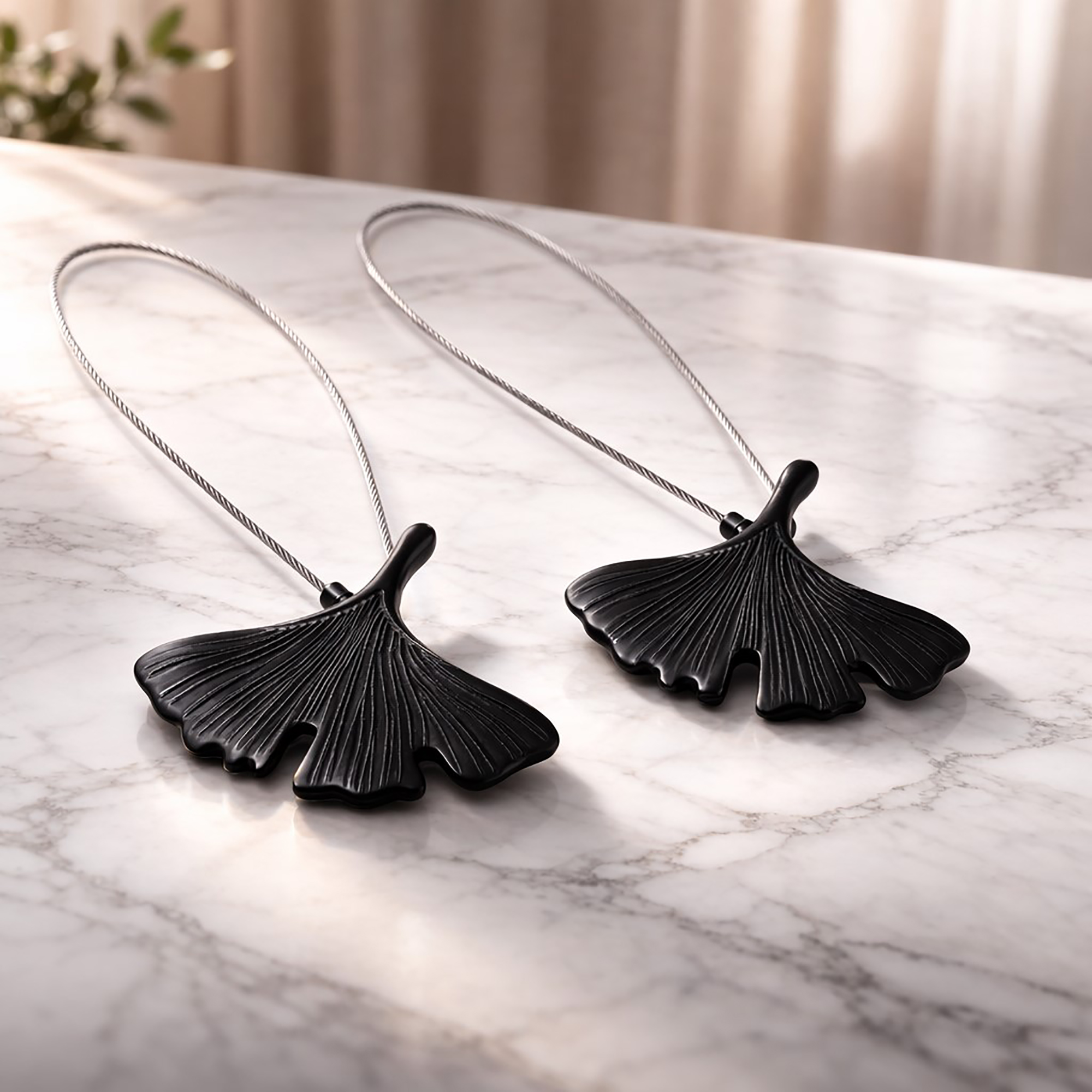"Two black metal ginkgo leaf magnetic curtain tiebacks displayed on a marble surface"