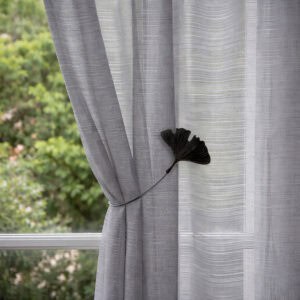 "Black ginkgo leaf magnetic tieback on grey textured curtains beside a garden window"