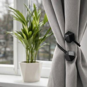 Black geometric tieback bundling a grey curtain near a sunlit window with indoor plant