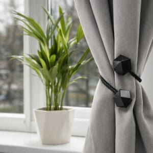 Black geometric tieback bundling a grey curtain near a sunlit window with indoor plant