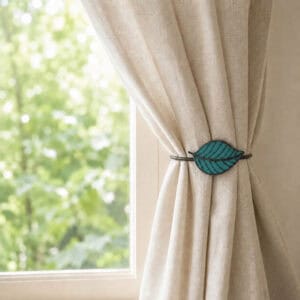 Teal leaf tieback holding a linen curtain back beside a sunny window
