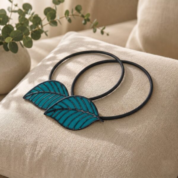 Two matching teal leaf tiebacks styled together on a linen cushion