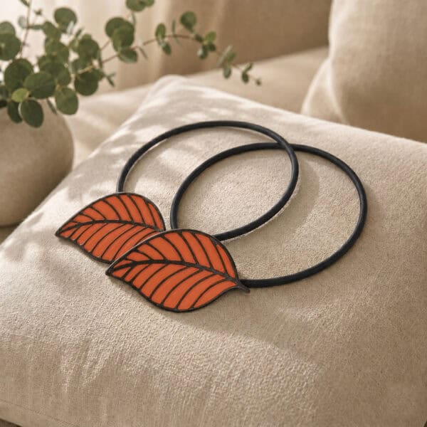 Two matching terracotta leaf tiebacks styled together on a linen cushion