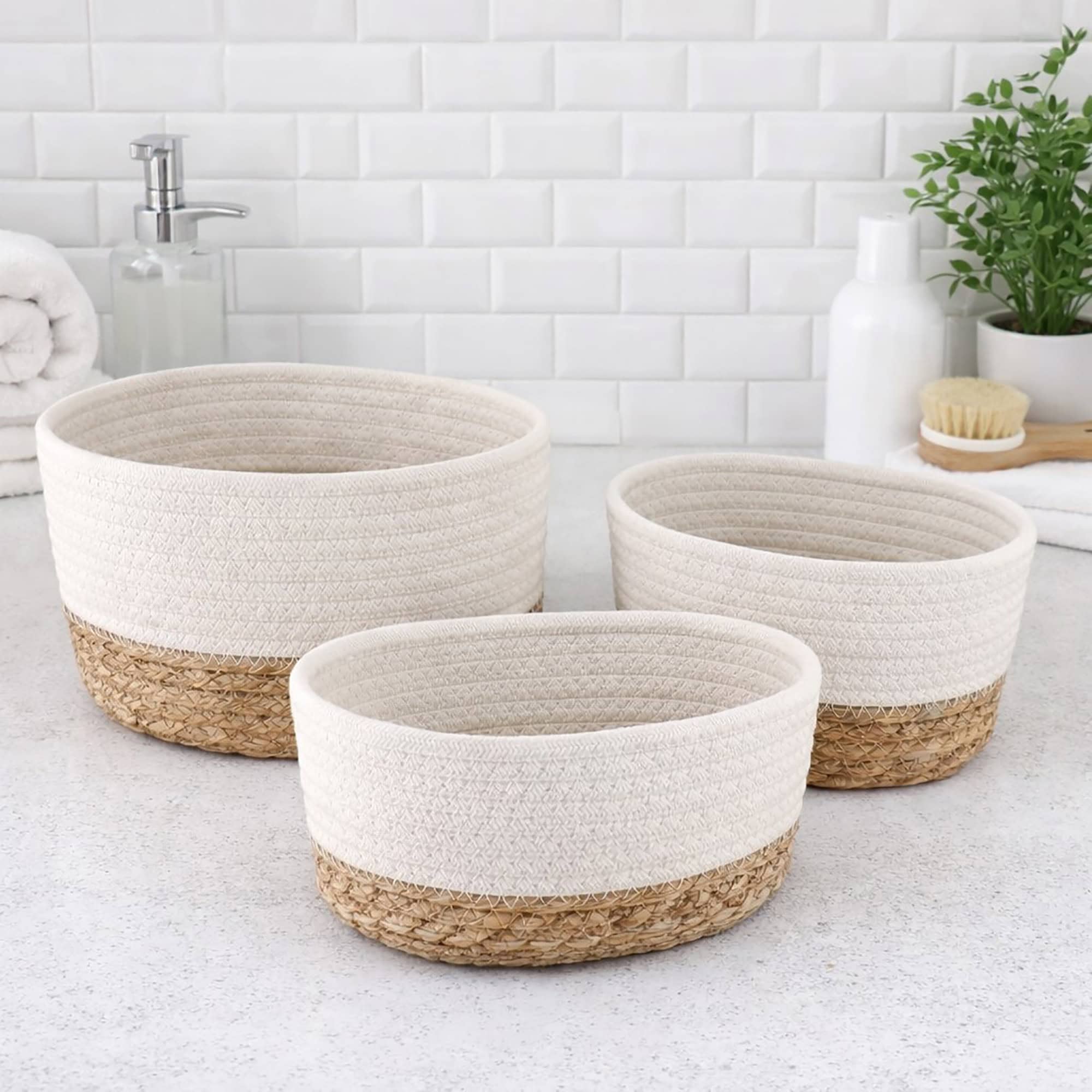 Three white cotton and seagrass oval baskets in graduated sizes displayed empty on a bathroom countertop.
