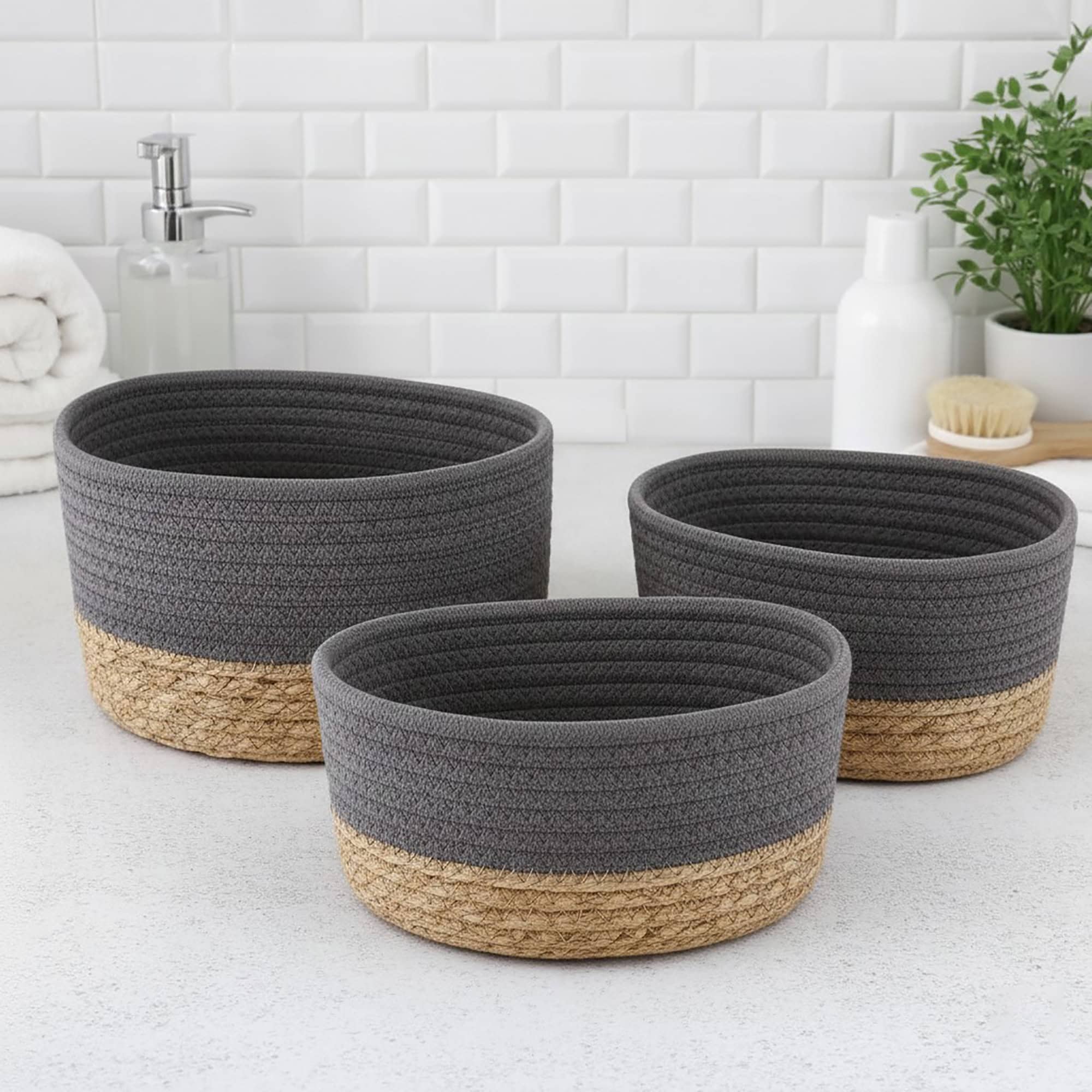 Three gray cotton and seagrass oval baskets in graduated sizes displayed empty on a bathroom countertop.