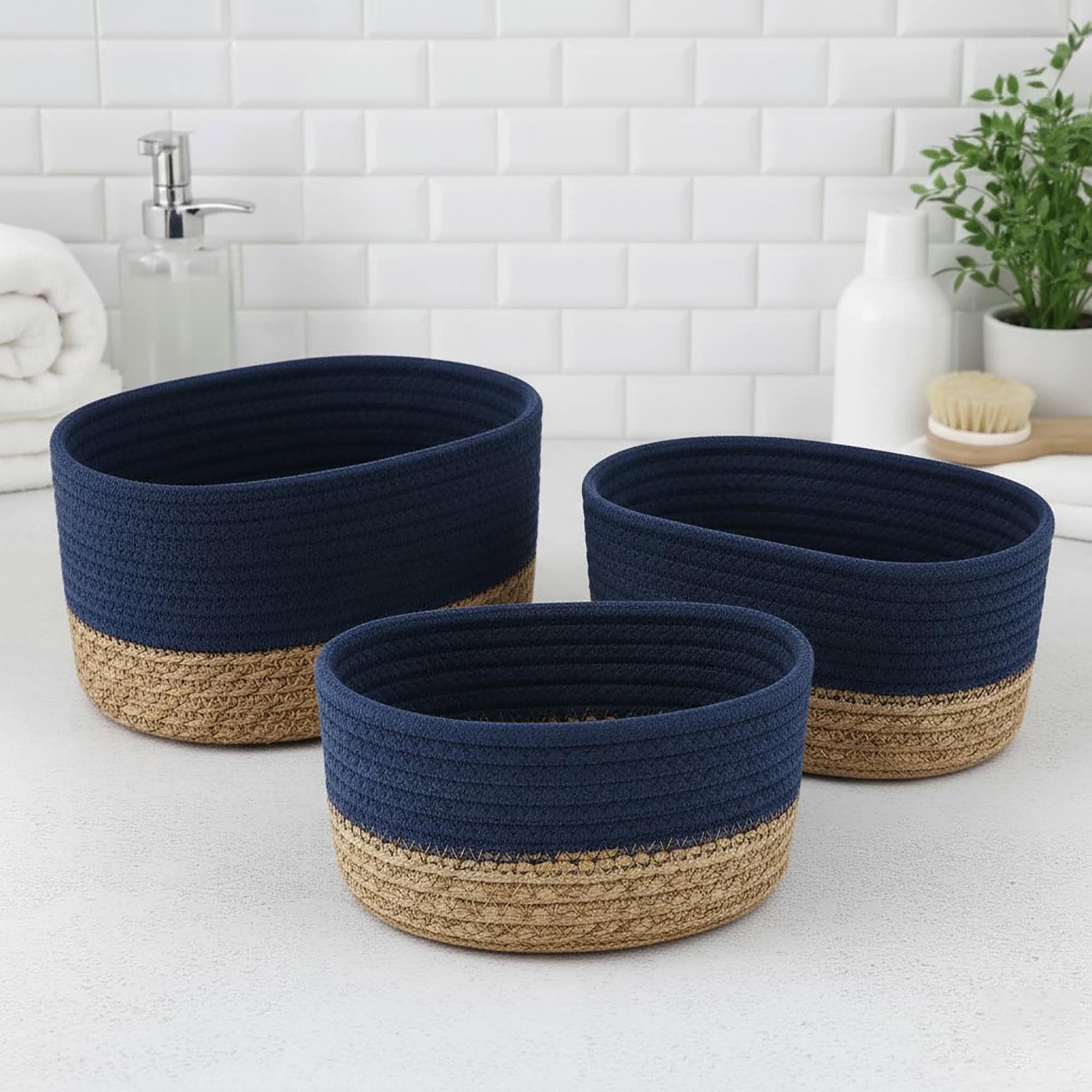 Three navy blue cotton and seagrass oval baskets in graduated sizes displayed empty on a bathroom countertop.