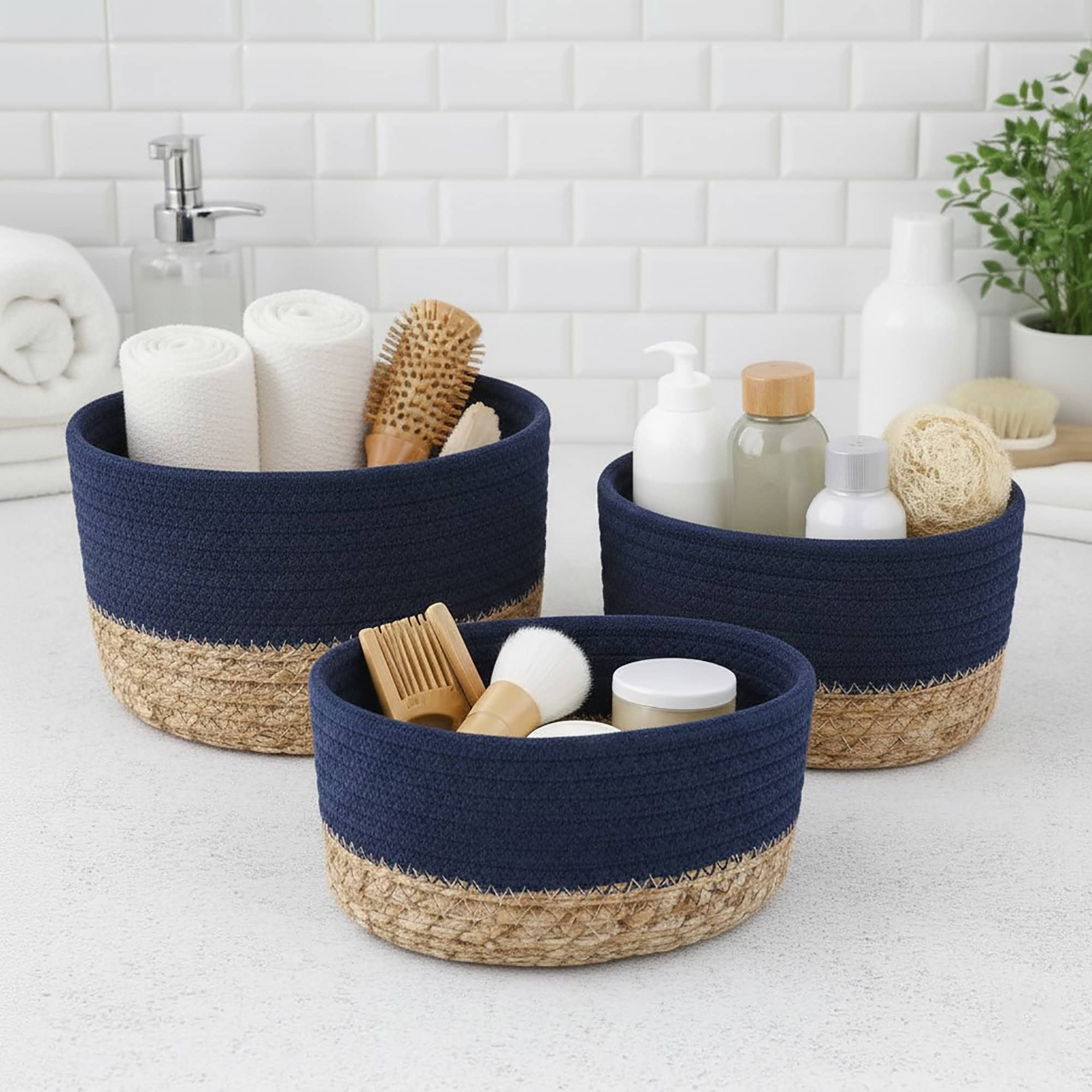 Three navy blue cotton and seagrass baskets filled with rolled towels, hairbrushes, skincare bottles, and a loofah on a bathroom countertop.