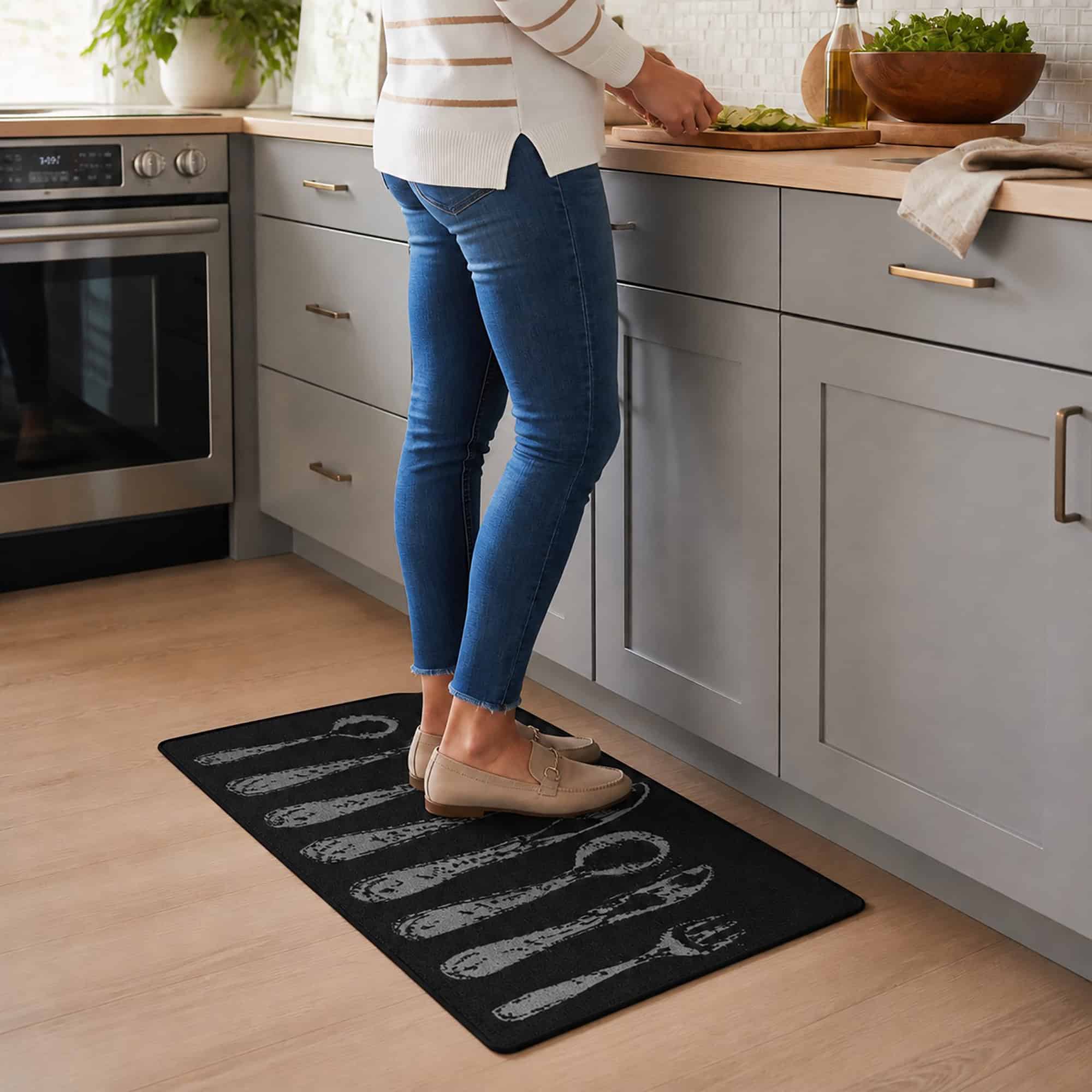 Person in jeans standing on a black cutlery print kitchen rug while prepping food at a gray counter, showing the mat in a real kitchen.