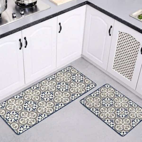Both kitchen mats laid on a gray floor in a white kitchen with arched cabinet doors, the runner and smaller mat showing their blue and gray pattern.