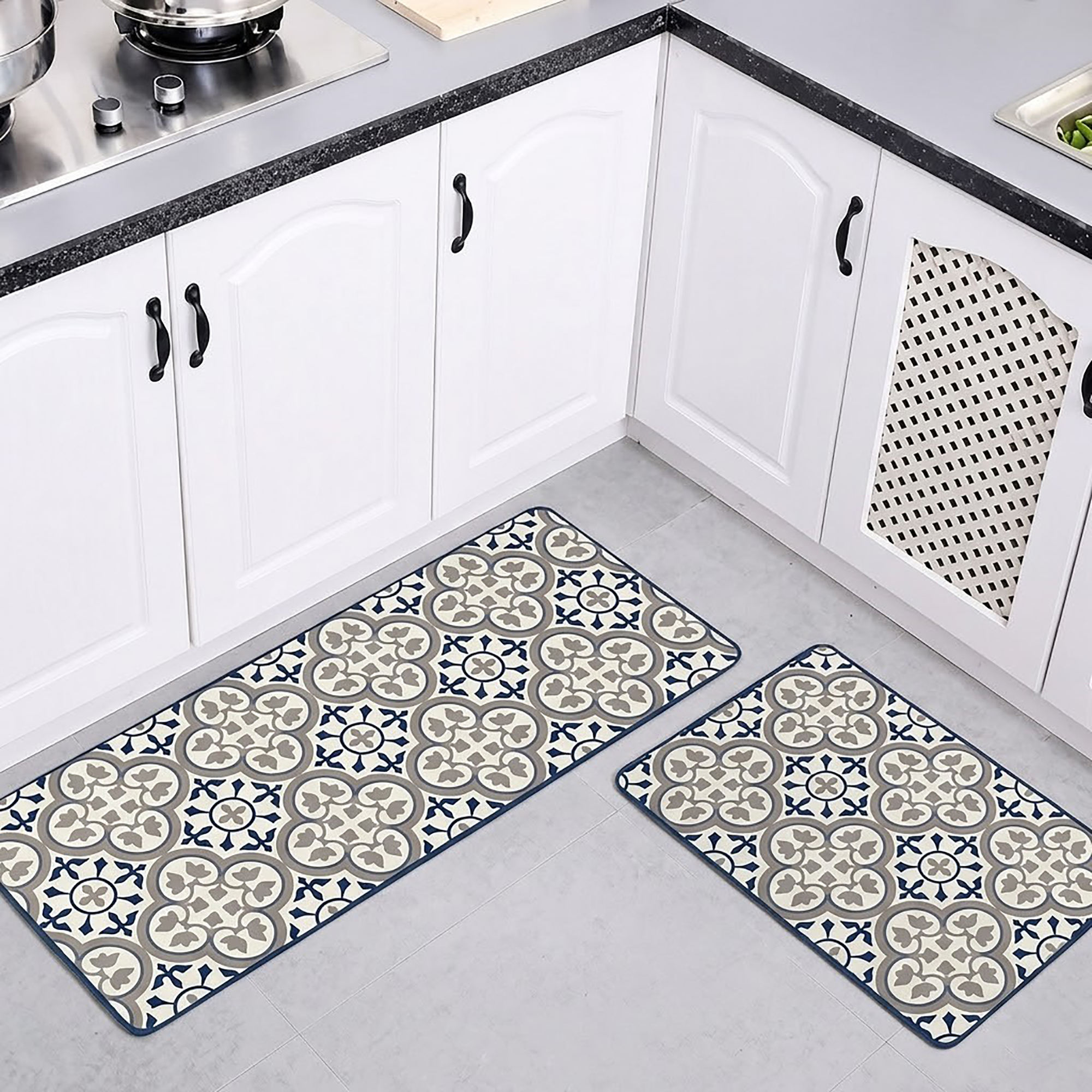Both kitchen mats laid on a gray floor in a white kitchen with arched cabinet doors, the runner and smaller mat showing their blue and gray pattern.