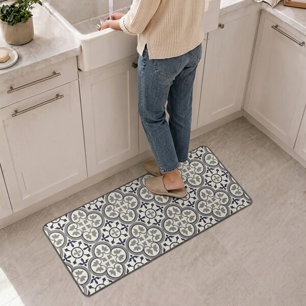 A person in slippers stands on the long kitchen runner before a white farmhouse sink, the runner stretching along the cabinets in blue and gray tile.