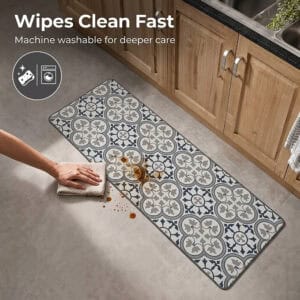 A hand wipes a brown spill from the long kitchen runner with a cloth, with icons indicating the runner is wipeable and machine washable.
