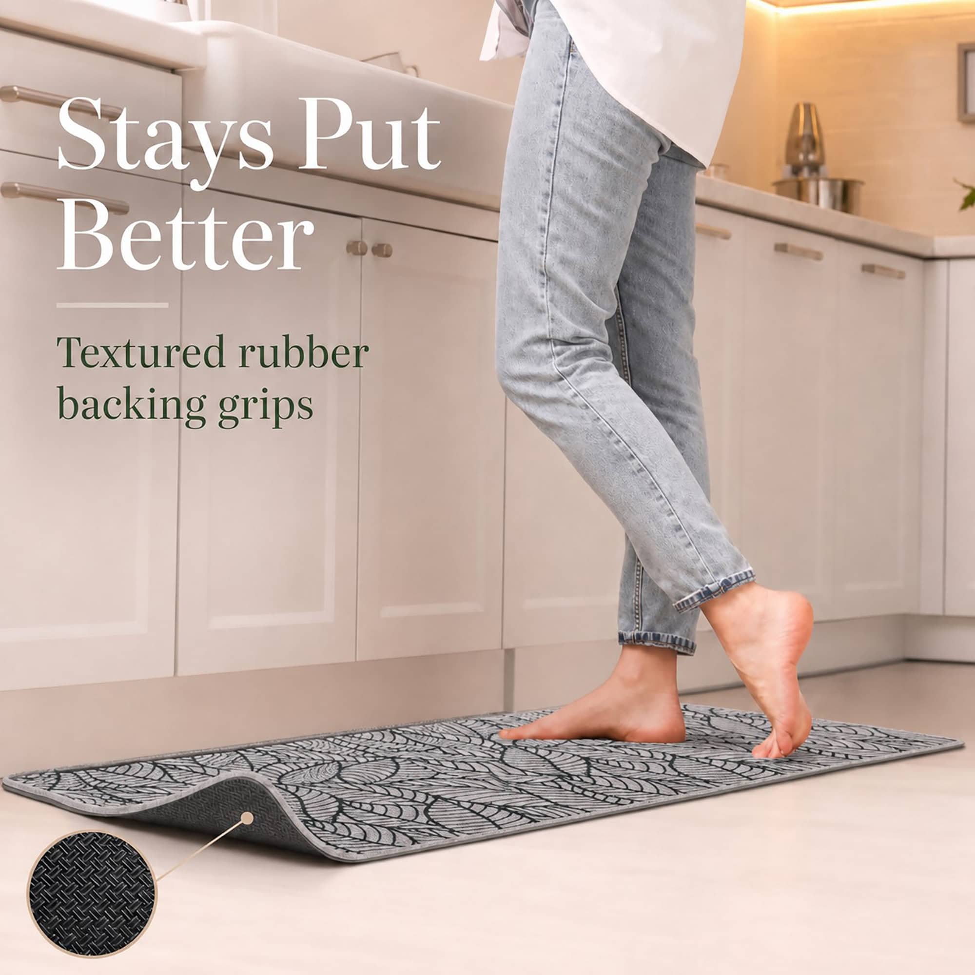 Person stepping onto a grey leaf-print kitchen runner, the lifted corner revealing the textured rubber backing that grips the floor.