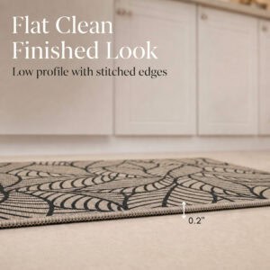 Side view of a beige leaf-print kitchen mat lying flat, showing its thin two-tenths of an inch profile with stitched edges.