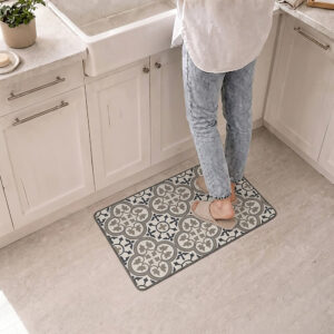 A person stands in slippers on the kitchen mat in front of a white farmhouse sink, the blue and gray tile pattern warming the space.