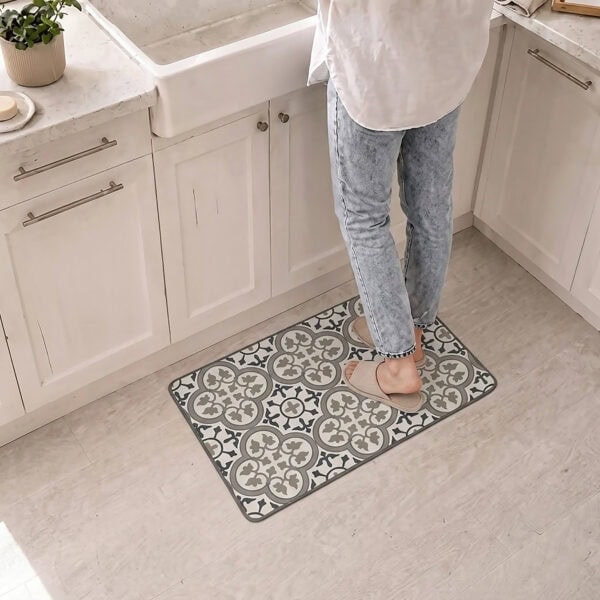 A person stands in slippers on the kitchen mat in front of a white farmhouse sink, the blue and gray tile pattern warming the space.