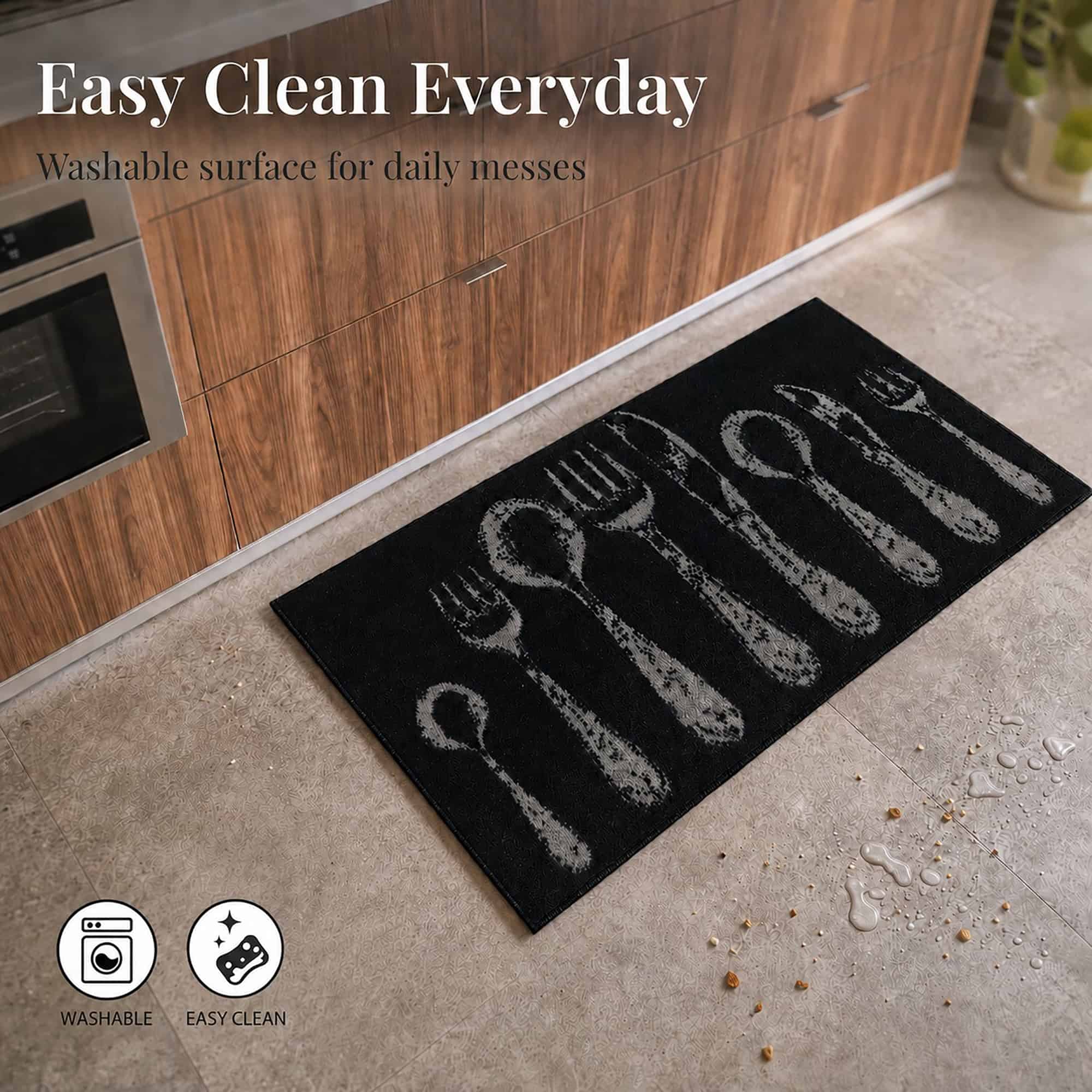 Black kitchen rug on a tiled floor beside scattered crumbs and a water spill, showing the washable surface for everyday messes.