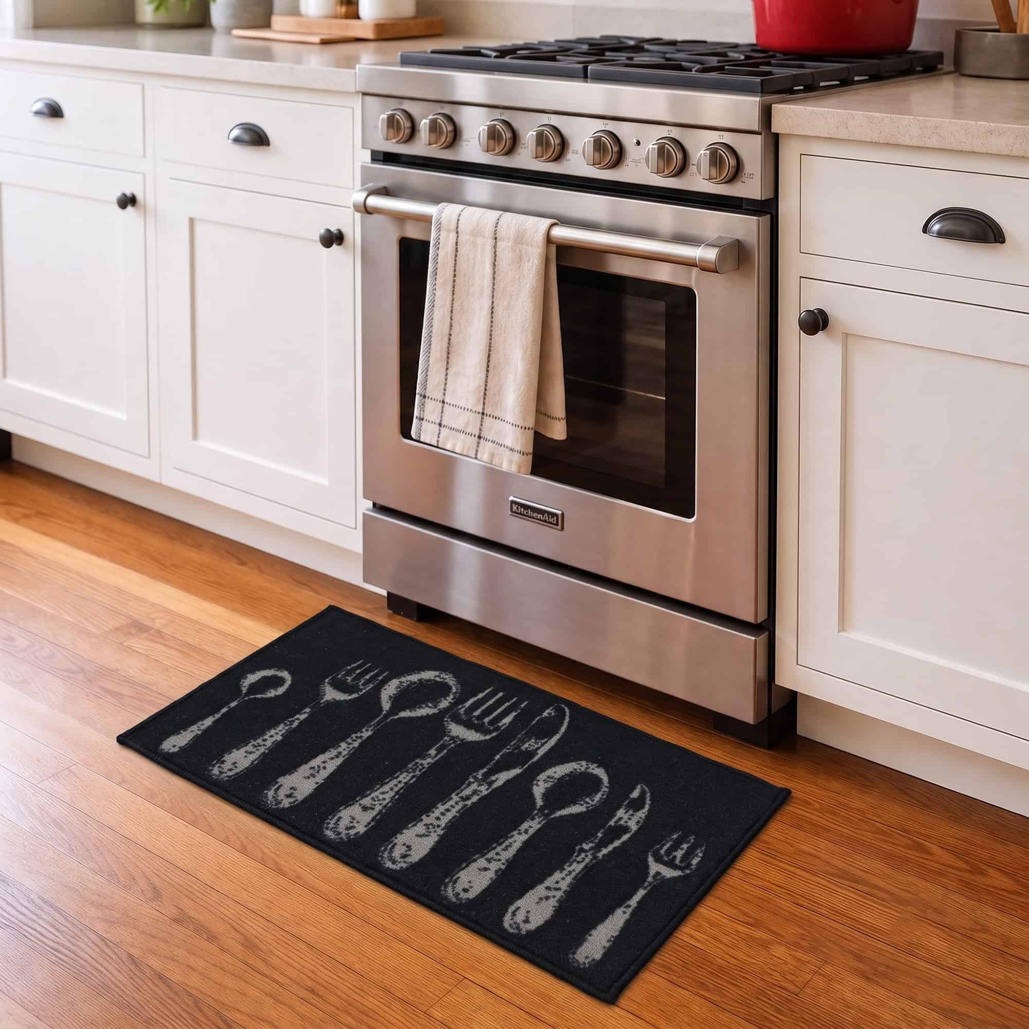 Black cutlery kitchen runner rug placed on a wood floor in front of a stainless steel range, styling the mat in a warm kitchen setting.