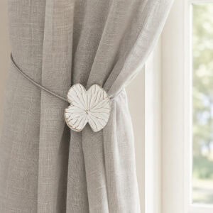 Lifestyle grège: White water lily magnetic tieback holding a light gray sheer linen curtain by a sunlit window