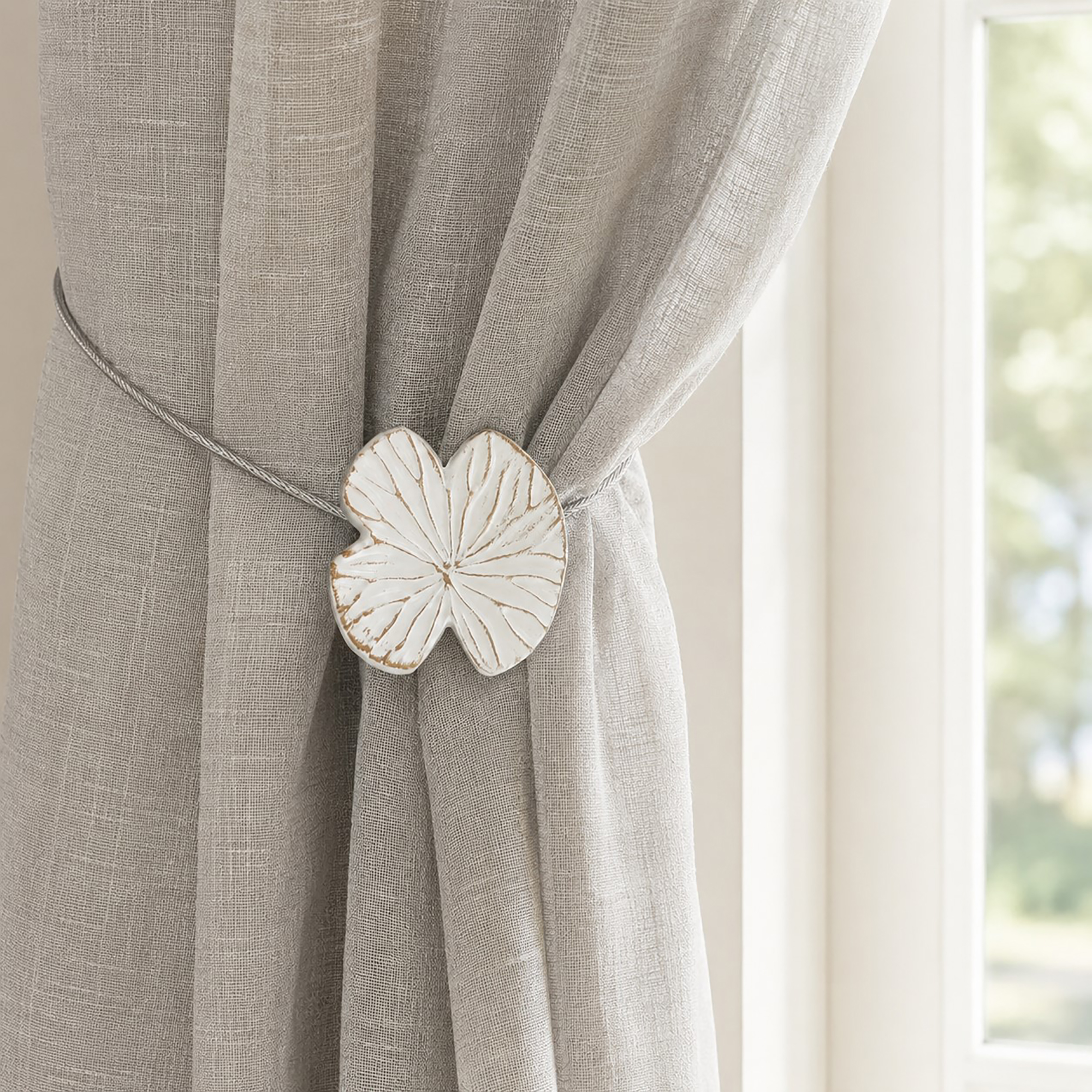 Lifestyle grège: White water lily magnetic tieback holding a light gray sheer linen curtain by a sunlit window