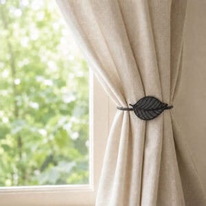 Gray leaf tieback holding a linen curtain back beside a sunny window
