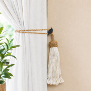 Black and silver leaf holdback gathering neutral drapes with a jute rope tassel tieback in a living room