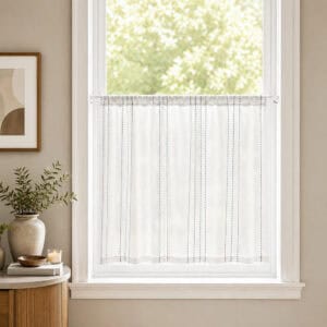 White cafe rod holding a sheer striped tier curtain across a bright kitchen window, styled with a green plant and light neutral decor for a farmhouse look.